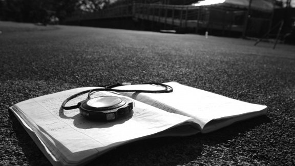 An open notebook lying on running track with a stopwatch resting on the left page